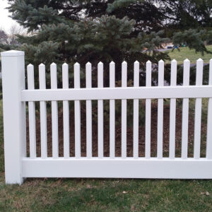 Milano white vinyl picket fence in front of pine trees